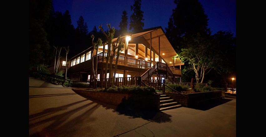 Architectural photography of large wood building in high mountains at dusk with trees and glowing lights
